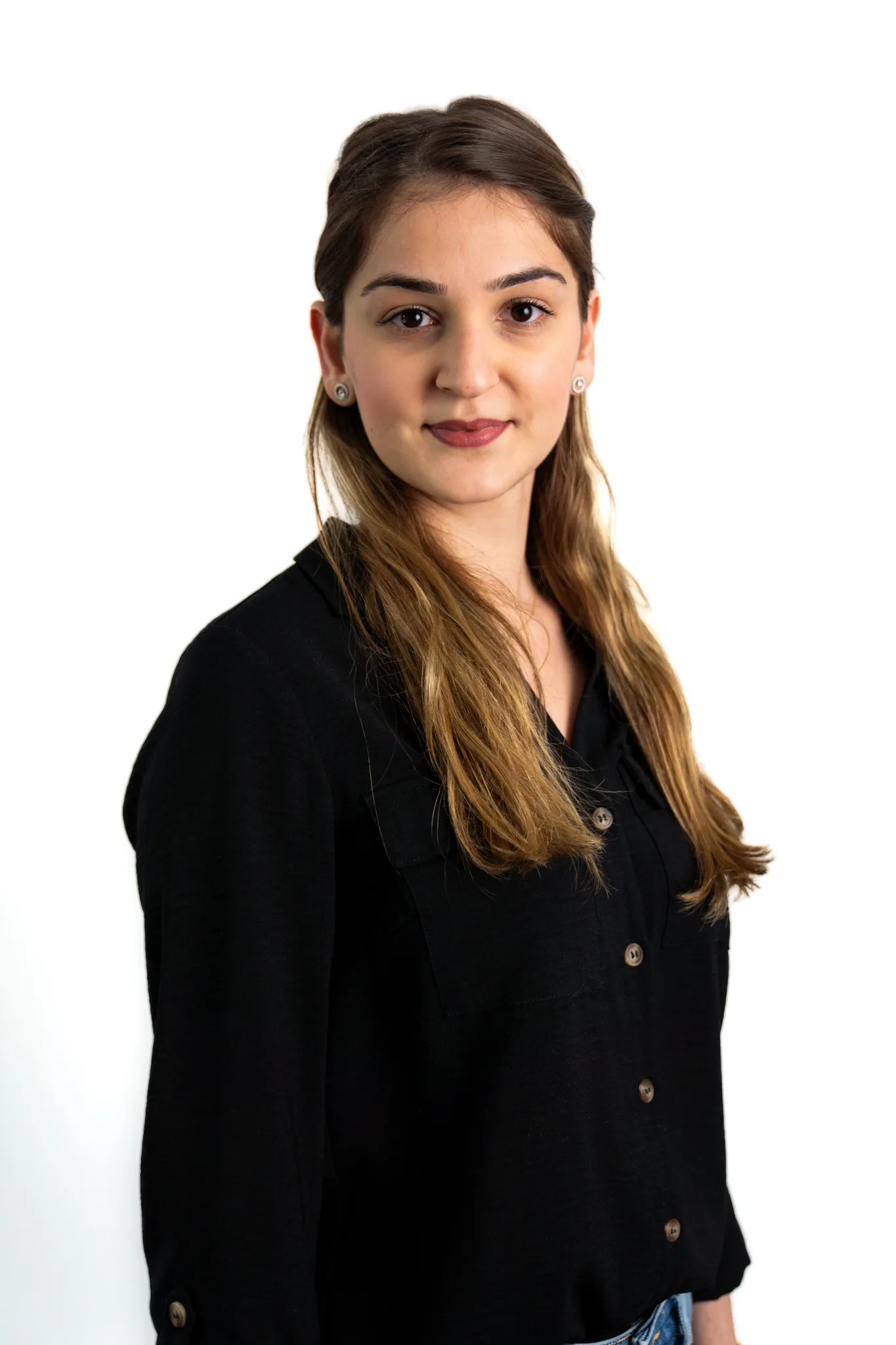 Porträt einer jungen Frau mit langen braunen Haaren, die in die Kamera blickt und leicht lächelt.