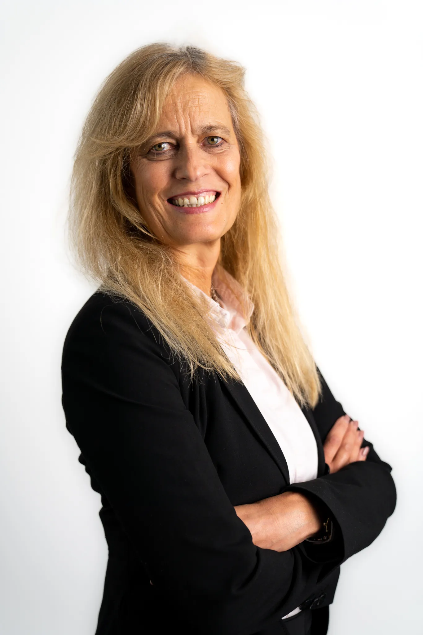 Porträt einer Frau mit langen blonden Haaren im schwarzen Blazer, die lächelnd mit verschränkten Armen in die Kamera schaut.