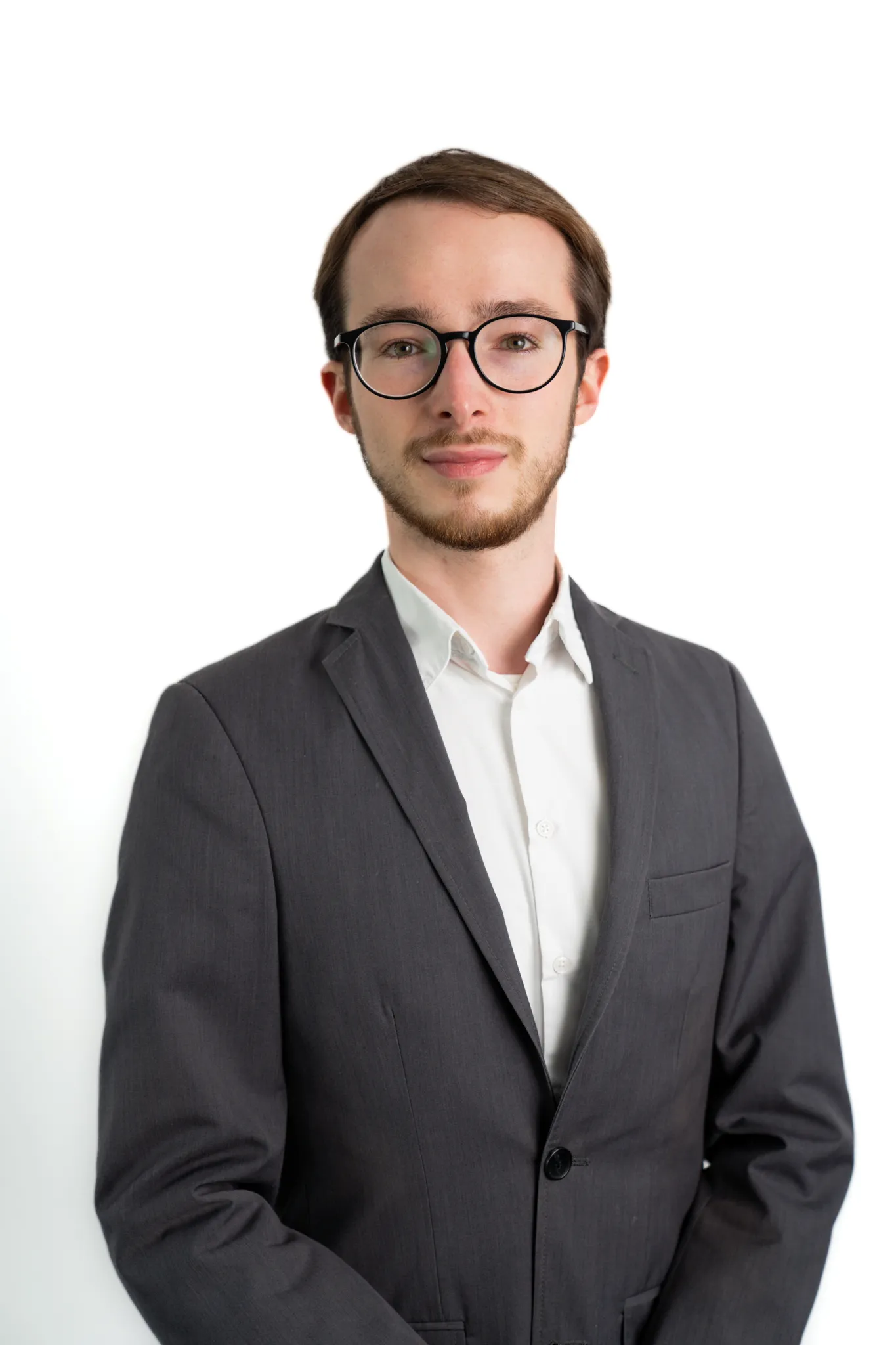 Porträt eines jungen Mannes mit Brille und Bart im grauen Anzug, der neutral in die Kamera schaut.