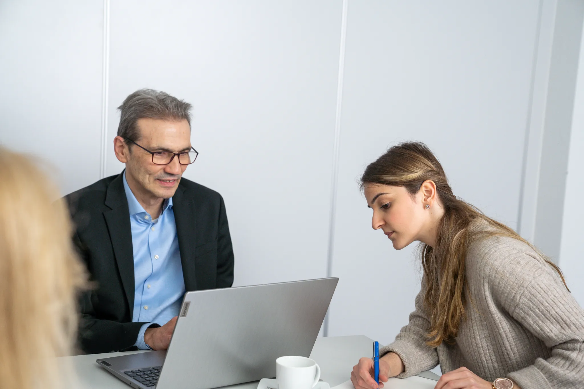 Mann und Frau sitzen zusammen an einem Tisch, der Mann zeigt etwas am Laptop.
