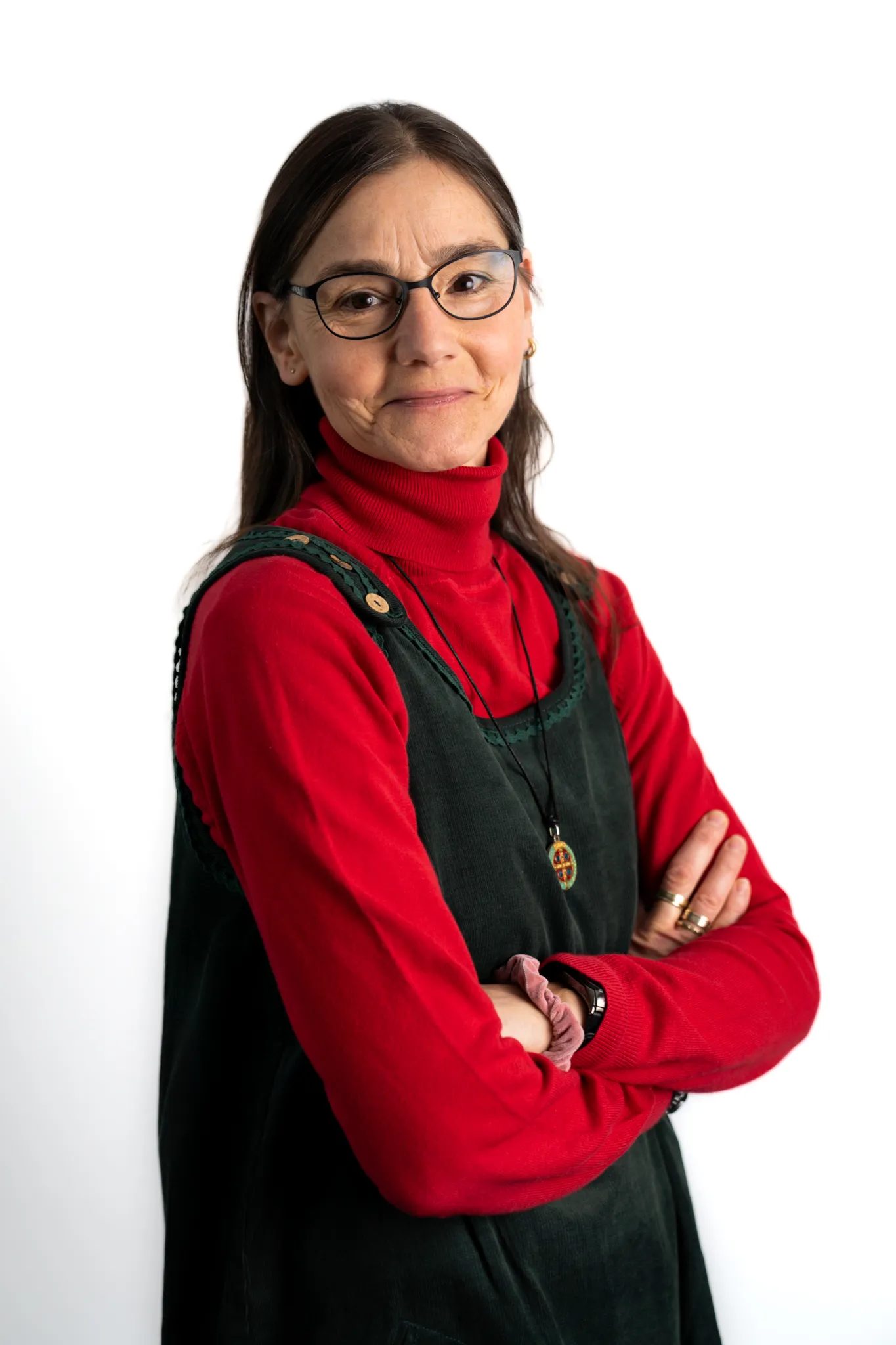 Porträt einer Frau mit Brille, rotem Rollkragenpullover und schwarzem Kleid, die mit verschränkten Armen lächelt.
