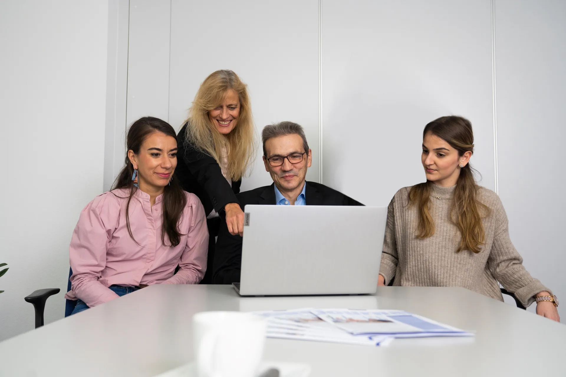 Vier Personen sitzen gemeinsam am Tisch vor einem Laptop und arbeiten zusammen.